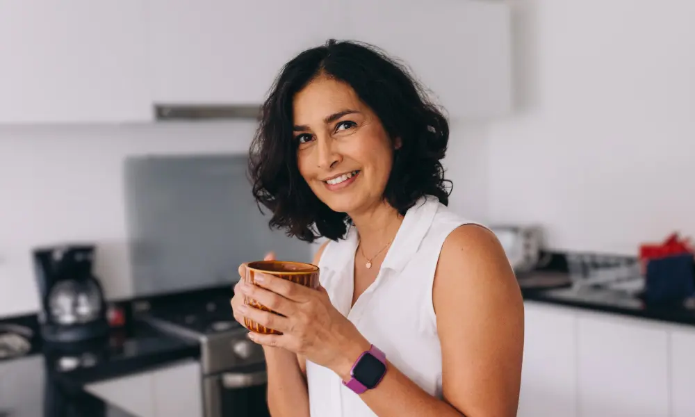 キッチンでほほ笑む女性。腕時計をつけている。忙しい中で英語学習をするイメージ。