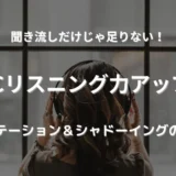 ヘッドフォンをつけて窓の外を見ながら英語音声を聞いている女性。集中してリスニング学習に取り組んでいる様子。