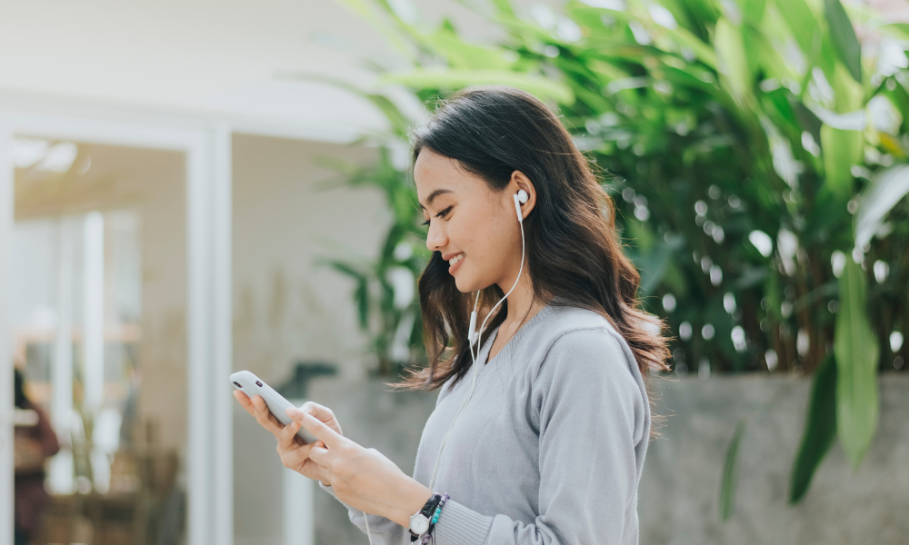 外でイヤホンをつけながら英語音声を聞く女性