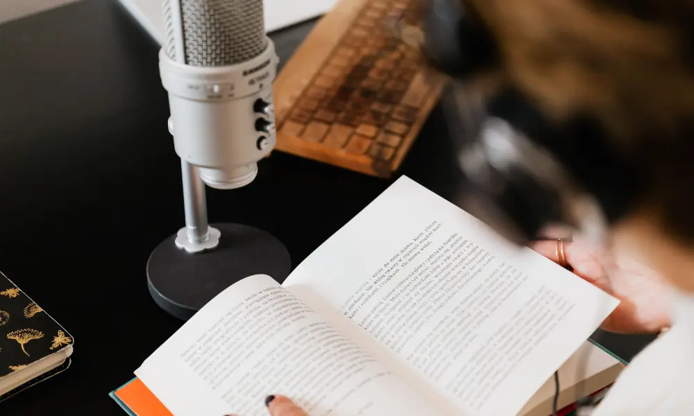 マイクの前で英語の本を開いている女性。録音しながら音読する様子