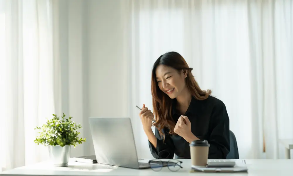 パソコンの前で小さくガッツポーズをする女性。達成感を感じている様子