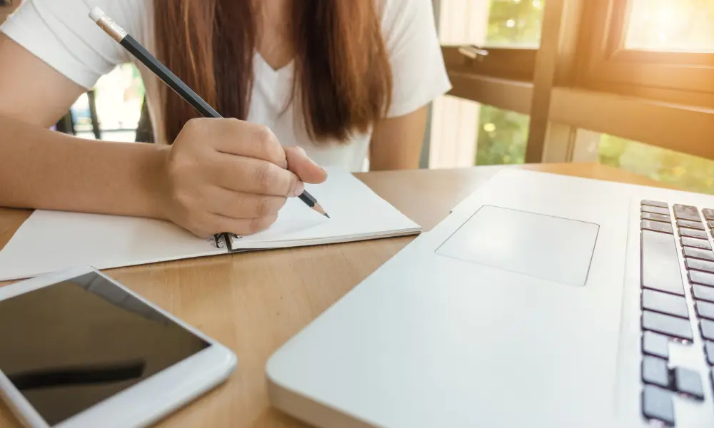 自然光の中でノートとスマホを使い、真剣にTOEICの勉強をしている女性のイメージ
