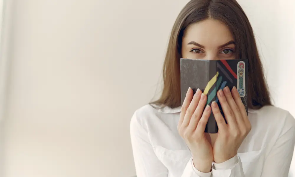 英語を話そうとして恥ずかしそうに本で顔を隠す女性。話すことに自信がない様子