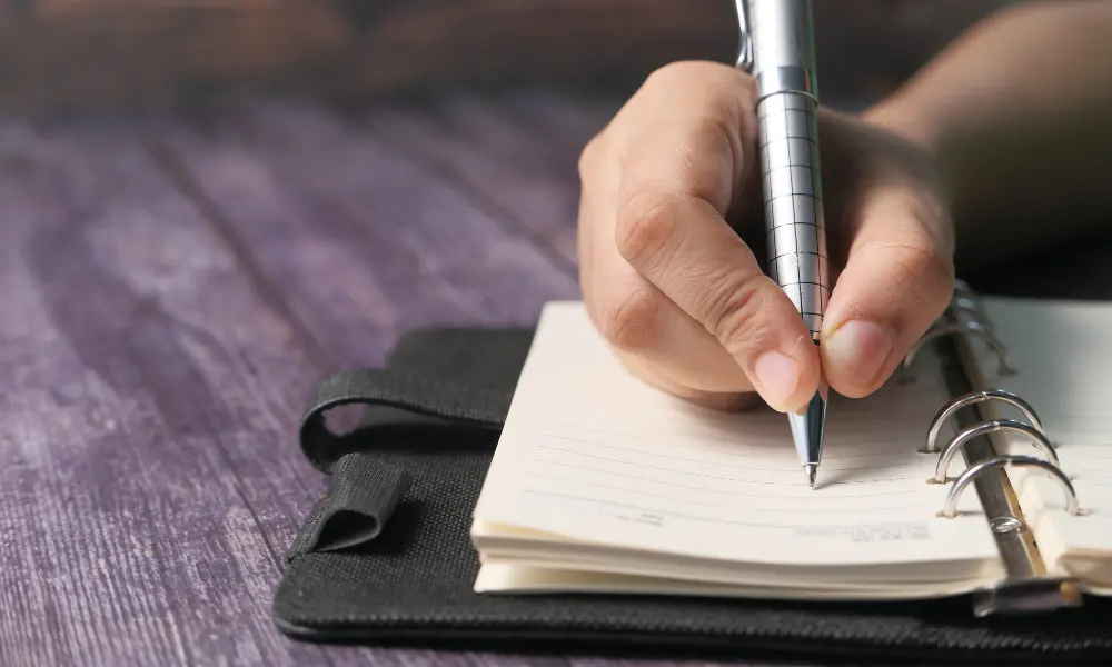 日常英会話のネタをメモするように、手帳に書き込む手元