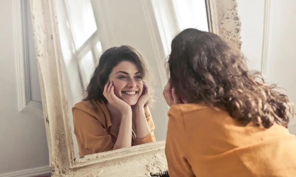 鏡越しに自分と笑顔で向き合う女性。人と比べず、自分自身を認めるスピーキングマインドを表現。
