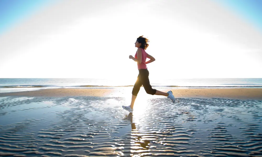 朝日が差し込む海辺を軽やかにランニングする女性。スピーキングに向けて前向きに一歩踏み出すイメージ。
