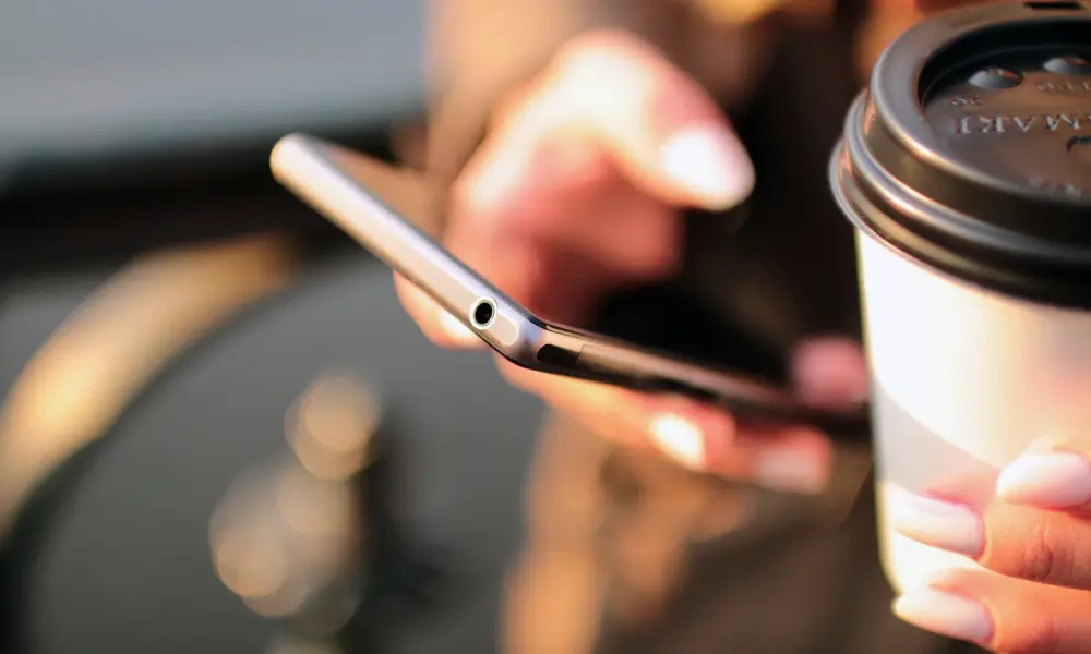 朝のひとときに、コーヒー片手でスマホをチェックする女性の手元。TOEIC前日の軽い復習をイメージさせる日常の風景。
