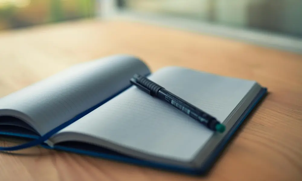 木目のデスクにノートとペンが置かれ、落ち着いた雰囲気で英語学習の準備をする様子。