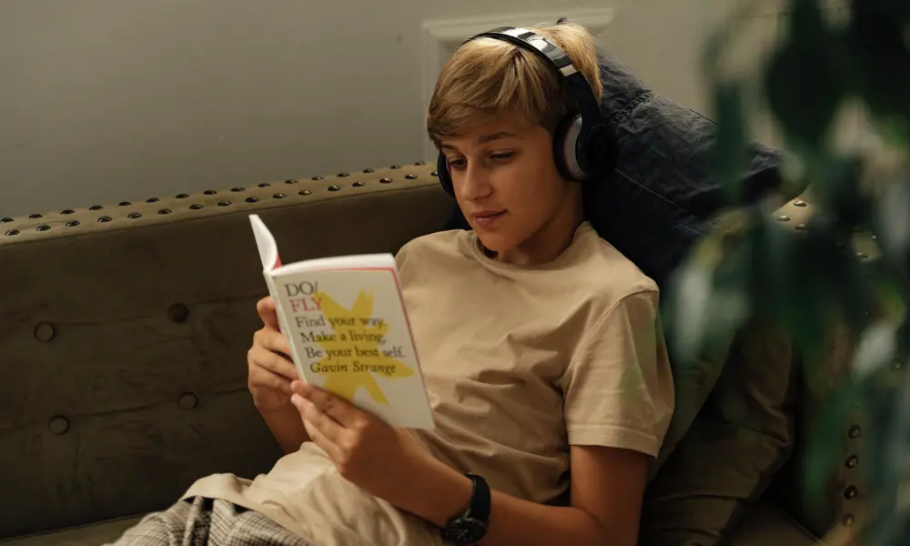 ソファでリラックスしながら本を開き、ヘッドフォンで音を聞いている様子。