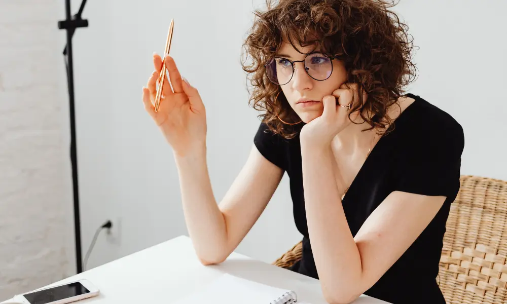 机に座り、ノートを前に英語日記について考えながらペンを回す女性