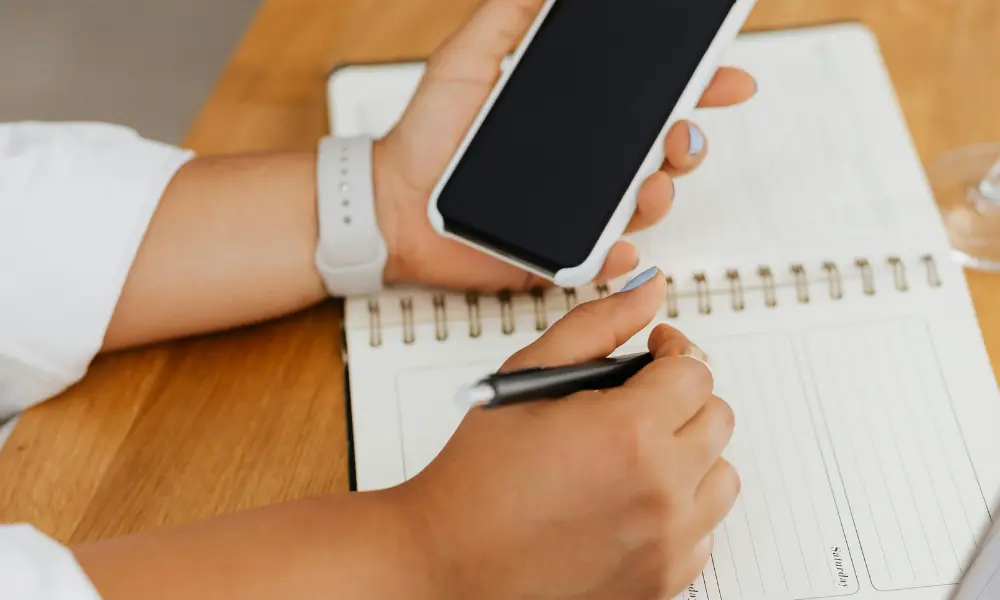 スマホを確認しながら、紙のダイアリーに英語日記を書こうとする手元